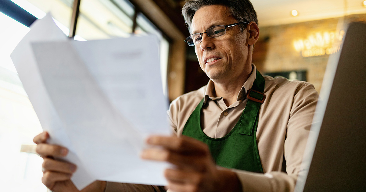 man looking at paperwork with laptop